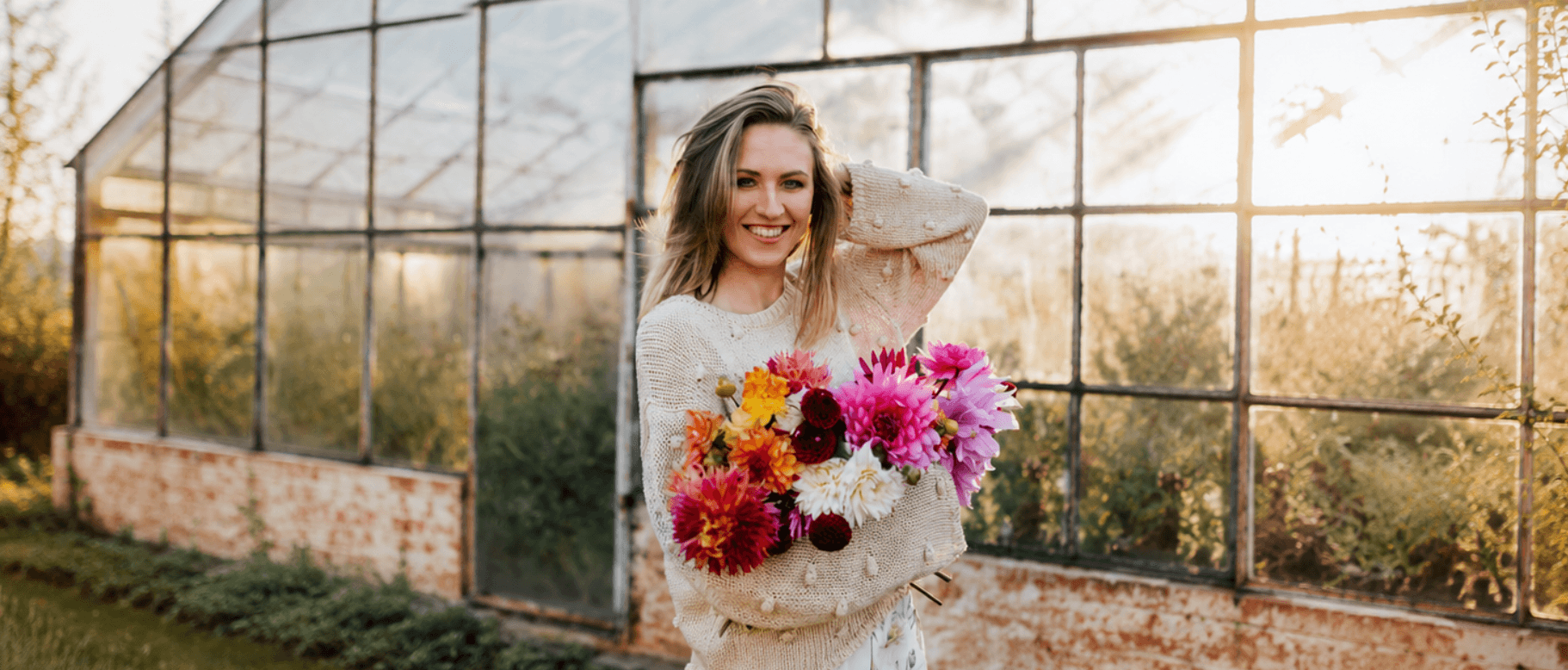 Creator holding a bouquet of dahlias outside a greenhouse at golden hour