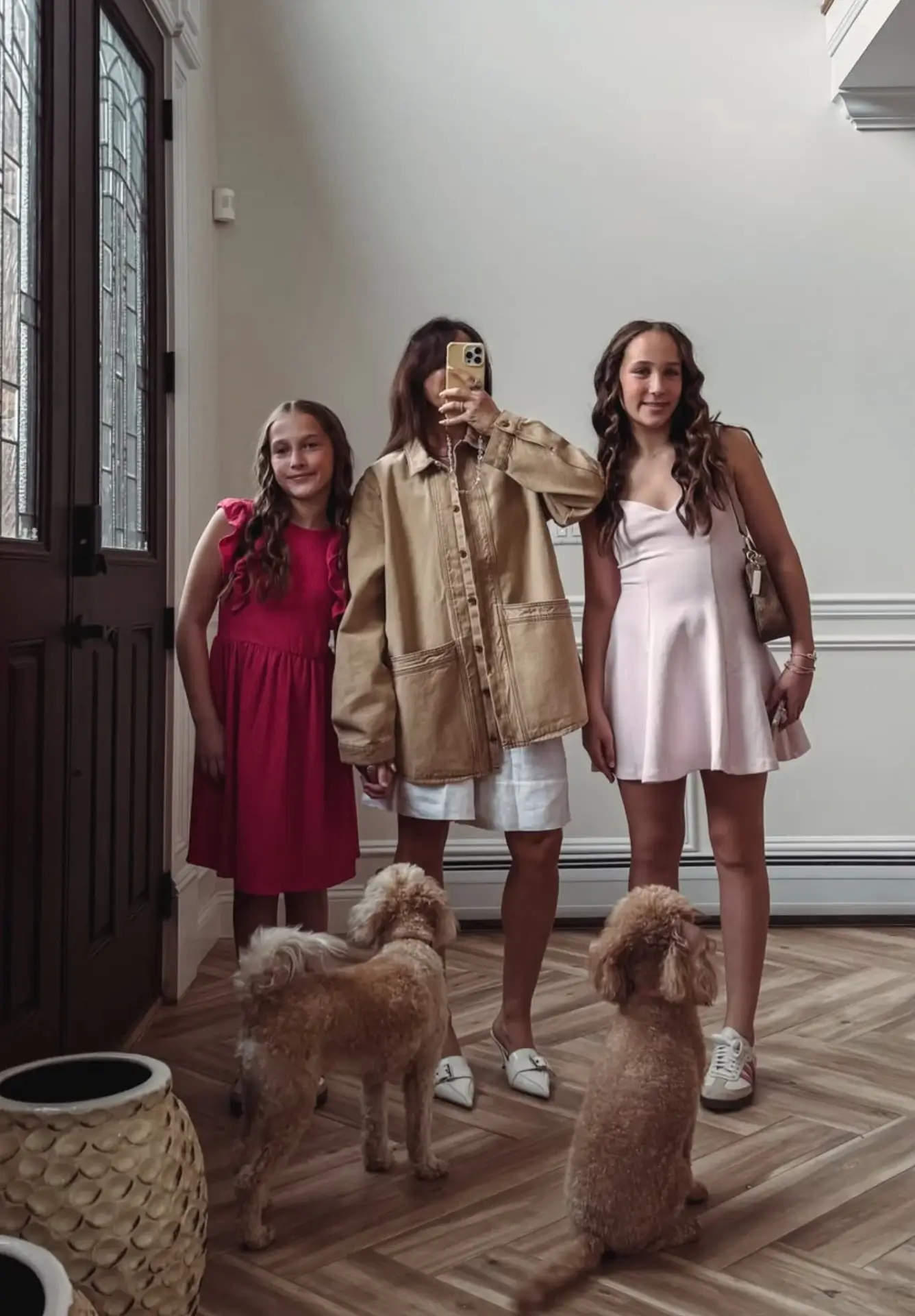 Three people taking a mirror selfie with two small dogs in a bright hallway